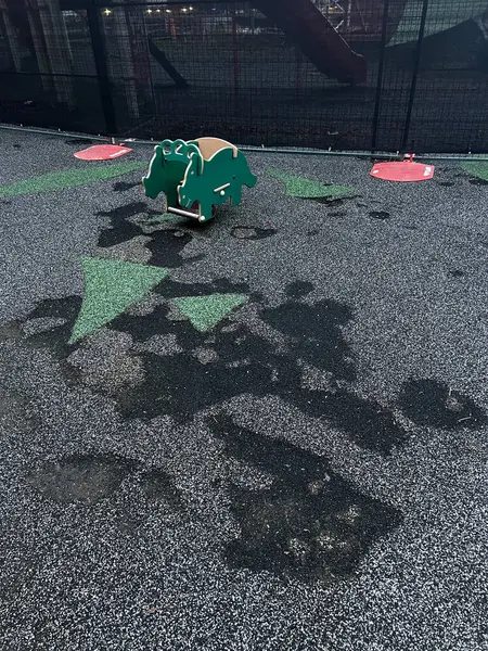 stock image This photo highlights a worn playground rubber surface, featuring green patterns with dark, damp patches that indicate wear and tear from frequent use or weather exposure