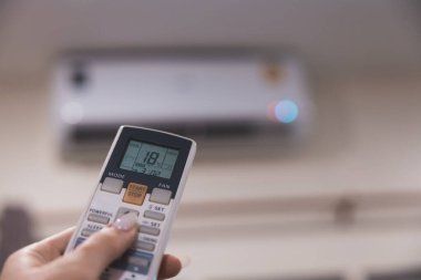 Klimanın uzaktan kumandası 18 'e ayarlı ve arka planda havalandırma ünitesi görünüyor.