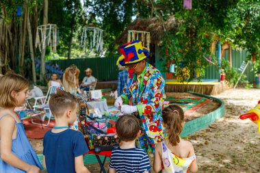 Ko Samui, Thailand - September 9,2024: A colorful clown entertains a group of children outdoors, creating a cheerful and engaging atmosphere clipart