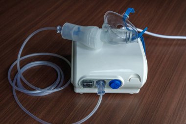 Solunum tedavisinde kullanılan ahşap bir yüzeye bağlı yüz maskesi ve borusu olan bir masa üstü nebulizatörü.