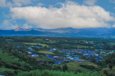 Kuzey Tayland 'da Mae Hong Son eyaletinin görkemli dağları tarafından desteklenen yuvarlanan tepelere dağılmış kendine özgü mavi çatıları olan Santichon Köyü' nün hava manzarası.