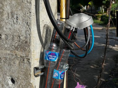 Ko Samui, Tayland - 26 Kasım 2024: Elektrik direğinde geçici elektrik kablosu koruması olarak kullanılan su şişeleri, doğaçlama güvenlik çözümünü gösteriyor