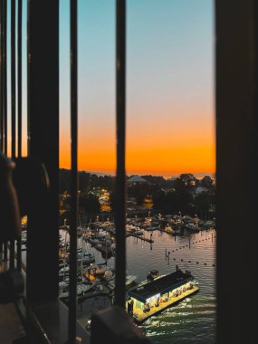 Sunset marina view through window bars, showing moored boats and illuminated floating dock against orange and blue twilight sky in Vancouver harbor clipart