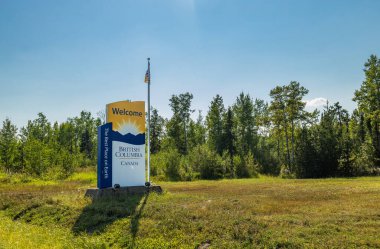 British Columbia, Kanada - 25 Ağustos 2022 İngiliz Kolombiyası için hoş geldin işareti dağların üzerinde gün doğumuyla birlikte yeşil orman arka planına sahip çimenlik alanda konumlanmış taşra logosu