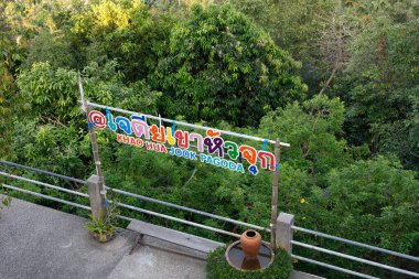 Viewing platform at Kao Hua Jook Pagoda in Ko Samui with a colorful sign displaying both Thai and English text, offering panoramic views of the island's hillside and coastline amid tropical vegetation clipart