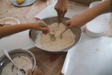 Metal bir kâseye un karıştıran çocuklarla yemek pişirme kulübü. Çoklu eller, hamur hazırlarken malzemeleri karıştırarak birlikte çalışır.