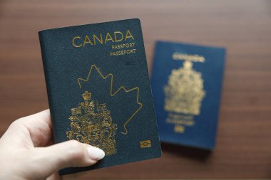Vancouver, Kanada - 18 Mart 2025: Koyu mavi bir Kanada pasaportu, üzerinde akçaağaç yaprağı ana hatları ve arması bulunan, tasarımın evrimini gözler önüne seren, altın işlemeli bir Kanada pasaportu