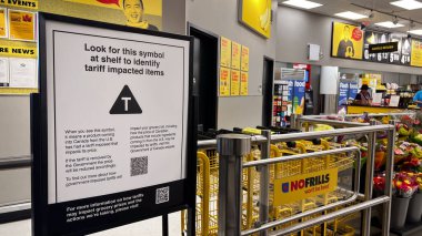 Vancouver, Kanada - 24 Temmuz 2025: Canlı bir No Frills mağazasının içinde, ABD 'nin Kanada ile ticaret savaşının ortasında ithalatından gelen fiyat değişikliklerine dikkat çeken T sembollü gümrük vergisi taşıyan bir tabela var