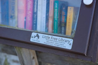 Vancouver, Kanada - 15 Eylül 2025: Renkli kitaplarla dolu camdan önü açık küçük bir kütüphane