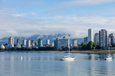 Serene Vancouver silueti sakin liman sularında süzülen yelkenliler, arka planda sisli Kuzey Sahili Dağları parçalı bulutlu gökyüzünün altında