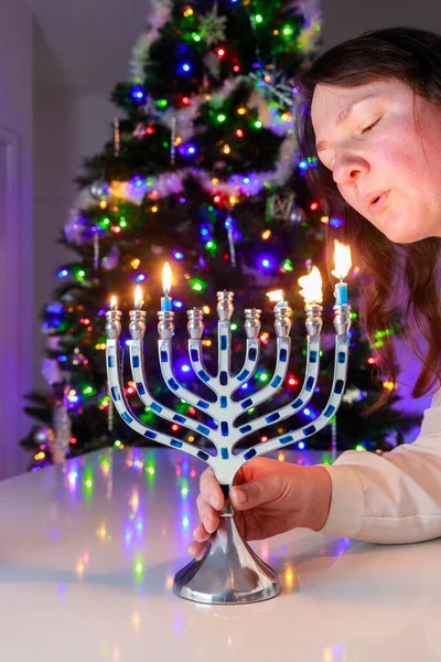 Jewish woman blows out the candles on the Hanukkah menorah with nine candles.