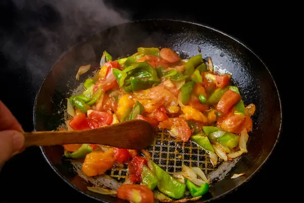 An iron skillet is used to stir-fry vegetables.