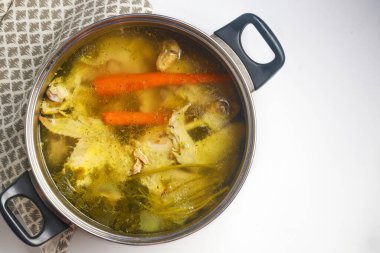 Et ve sebzelerle tavuk çorbası pişirmek için metal bir tencere kullanmak..