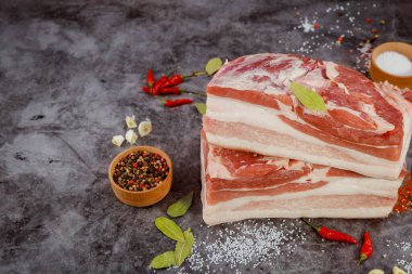 Kırmızı biber, biber ve aromatik otlarla çevrili koyu bir yüzeye yerleştirilmiş iki kalın domuz göbeği yemek pişirmek için kırsal bir ortam yaratıyor..