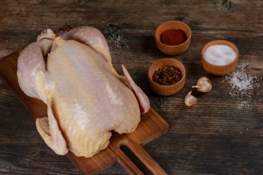 Tüm çiğ tavuk ahşap kesim tahtasına yerleştirilmiş, baharat ve sarımsak kâseleriyle çevrili. Kırsal mutfak ayarları aşçılık hazırlıklarını vurguluyor.
