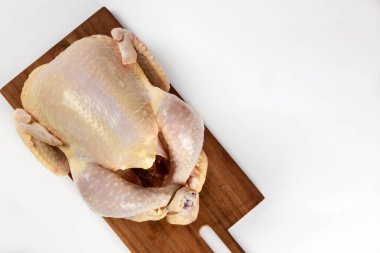 Whole chicken placed on wooden cutting board, showcasing its pale skin and raw form. Setting well-lit, indicating clean kitchen atmosphere suitable for cooking. clipart