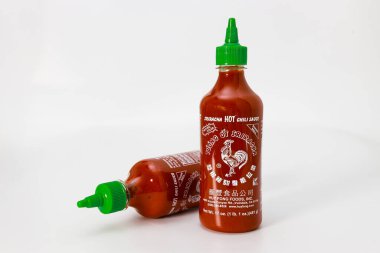 February 4, 2023. Spartanburg, SC USA. Bright red bottles of hot chili sauce Sriracha with green nozzles placed on white surface. clipart