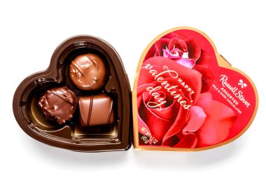 July 6, 2023. Spartanburg, SC USA. Heart-shaped box filled with assorted chocolates sits open, showcasing three delicious pieces. Box decorated with vibrant rose design, perfect for Valentines Day. clipart