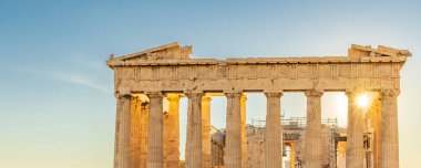 Sun hiding behind the columns of the Parthenon temple at Acropolis site on a sunny evening in Athens Greece