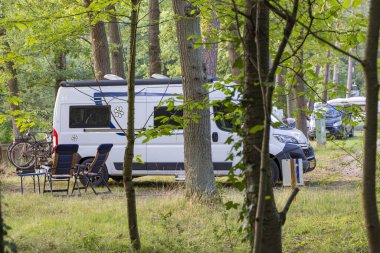 Kamp alanındaki ağaçlar arasında piknik masası ve sandalyeli bir kamp otobüsü.
