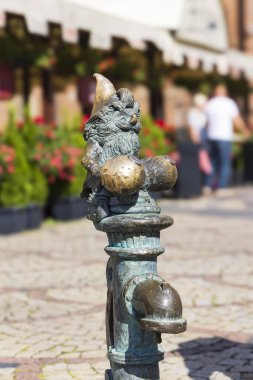 Wroclaw, Polonya - 20 Temmuz 2023: Wroclaw tarihinin başkenti Silezya ve Polonya 'nın cüce şehrindeki pazar meydanında su pompasının üzerinde oturan cüce heykeli.