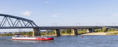 Nijmegen, Hollanda - 24 Eylül 2023: Güneşli bir sonbahar gününde Waal nehrindeki köprüden geçen kargo teknelerinin manzaralı manzaralı Nijmegen şehri.