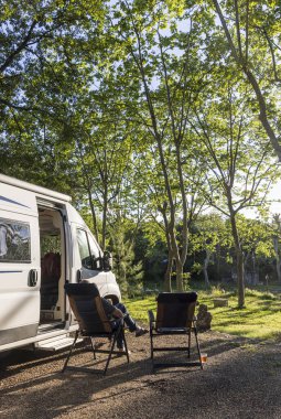 Güneşin altında bir sandalyede kamp alanındaki bir sürü ağacın yanında dinlenmek.