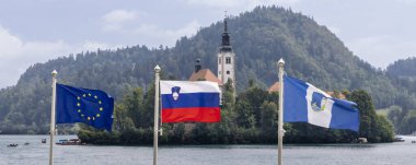 Slovenya 'nın Gorenjska bölgesinde Slovenya, AB ve Bled' in bayraklarıyla resmi Bled adası ve kalesi önünde Bled kenti