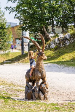 Slovenya 'nın Triglav Ulusal Parkı' ndaki Bohinj yakınlarındaki Vogel kayak merkezinde tahta keçi heykeline binen çocuklar yaz mevsiminde oturuyorlar