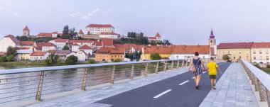 Anne ve çocuk gün batımında Slovenya 'nın Styria bölgesinde Drava riverin Ptuj üzerindeki yaya köprüsünden Ptuj' a doğru yürüyorlar.