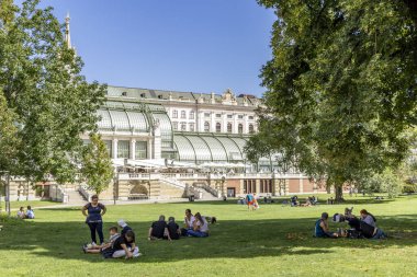Viyana, Avusturya - 7 Eylül 2024: Ağaçların gölgesinde dinlenen turist ve Viyana 'nın başkenti Avusturya' nın arka planında Kelebek evi