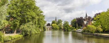 Flanders Belçika 'nın Brugge şehrinde önplanda renkli çiçekli Minnewater gölü ve şatosu