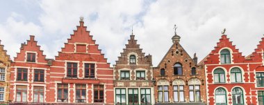 Belçika 'nın Brugge kentindeki bulutlu gökyüzünün önündeki büyük pazar meydanı boyunca uzanan teraslı gabya evleri ve restoranların panoramik manzarası