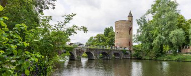 Brugge, Belçika - 4 Haziran 2025: Begijnenvest 'ta Minnewater Gölü boyunca Silah Gücü Kulesi (Poertoren) ve Belçika' nın Brugge şehrinin tarihi merkezinde Aşıklar Köprüsü