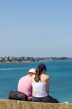 Manzaranın keyfini çıkaran genç turist çifti Fransa 'nın Normandiya kıyısındaki St. Malo şehir duvarını oluşturuyor.