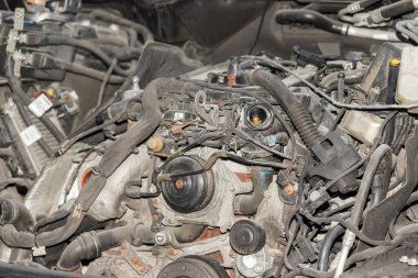 Bir tamir atölyesinde parçalanmış bir araba motorunun yakın çekim görüntüsü. Mekanik detaylar ve otomotiv bakım işlemleri gösteriliyor.