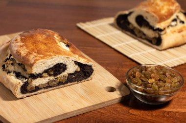 Afyon tohumu ve bambu kesme tahtasının üzerinde kuru üzümle yarı iştah açıcı bir rulo kes ve koyu ahşap bir masada Makisu ile kuru üzümle dolu bir kase.