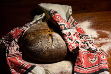 Kırmızı süslemeli havluya sarılı fırınlanmış ekmek ekmeği koyu ahşap bir masaya serpiştirilmiş.