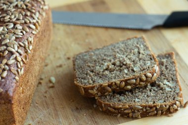 close-up of whole grain bread and cut pieces of bread and with a knife - on a wooden cutting board