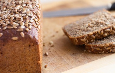 close-up of whole grain bread with sunflower seeds - on a blurred background of cut pieces and a wooden cutting board
