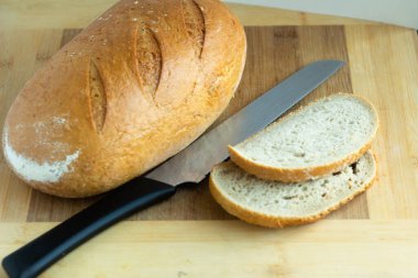 white wheat bread with slanting cuts with cut pieces and a knife - on a wooden background