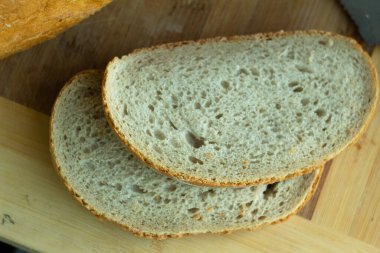 ruddy wheat bread with slanting cuts and cut pieces of bread - on a light wooden background top view
