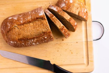 photography whole grain bread which is sliced on a wooden cutting board with a knife - on a white background top view