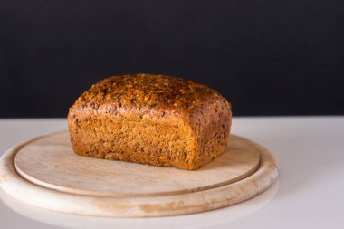 rye cereal bread with different seeds on a round wooden cutting board - on a white table with a gray fn