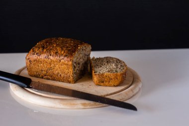 healthy cereal bread sliced on a wooden cutting board with a knife - on a white table with a black background