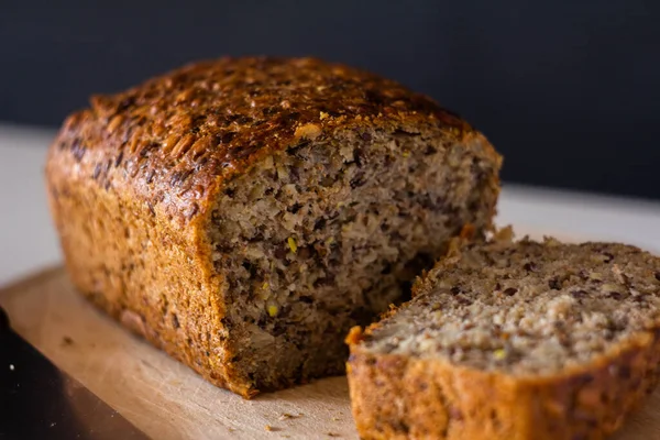 bread with different seeds sliced on a wooden cutting board - on a white table with a dark background
