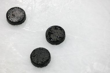 Black ice hockey rubber pucks set of 3 laying on Ice. Photo taken in indoor Ice hockey rink arena clipart