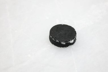 Small Black Ice Hockey puck laying on skated ice. Photo taken in indoor arena. clipart