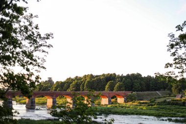 Venta nehri üzerinde eski kırmızı tuğlalı bir köprü olan ağaç manzarası. Fotoğraf Kuldiga 'da çekildi.