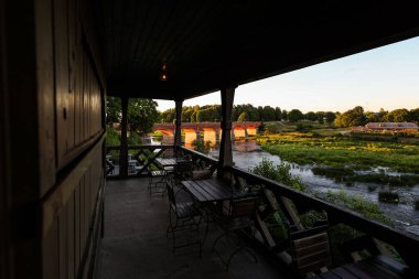 Venta üzerindeki eski, tarihi kırmızı tuğla köprü, sol tarafında kafe var. Fotoğraf gün batımından hemen sonra çekildi..